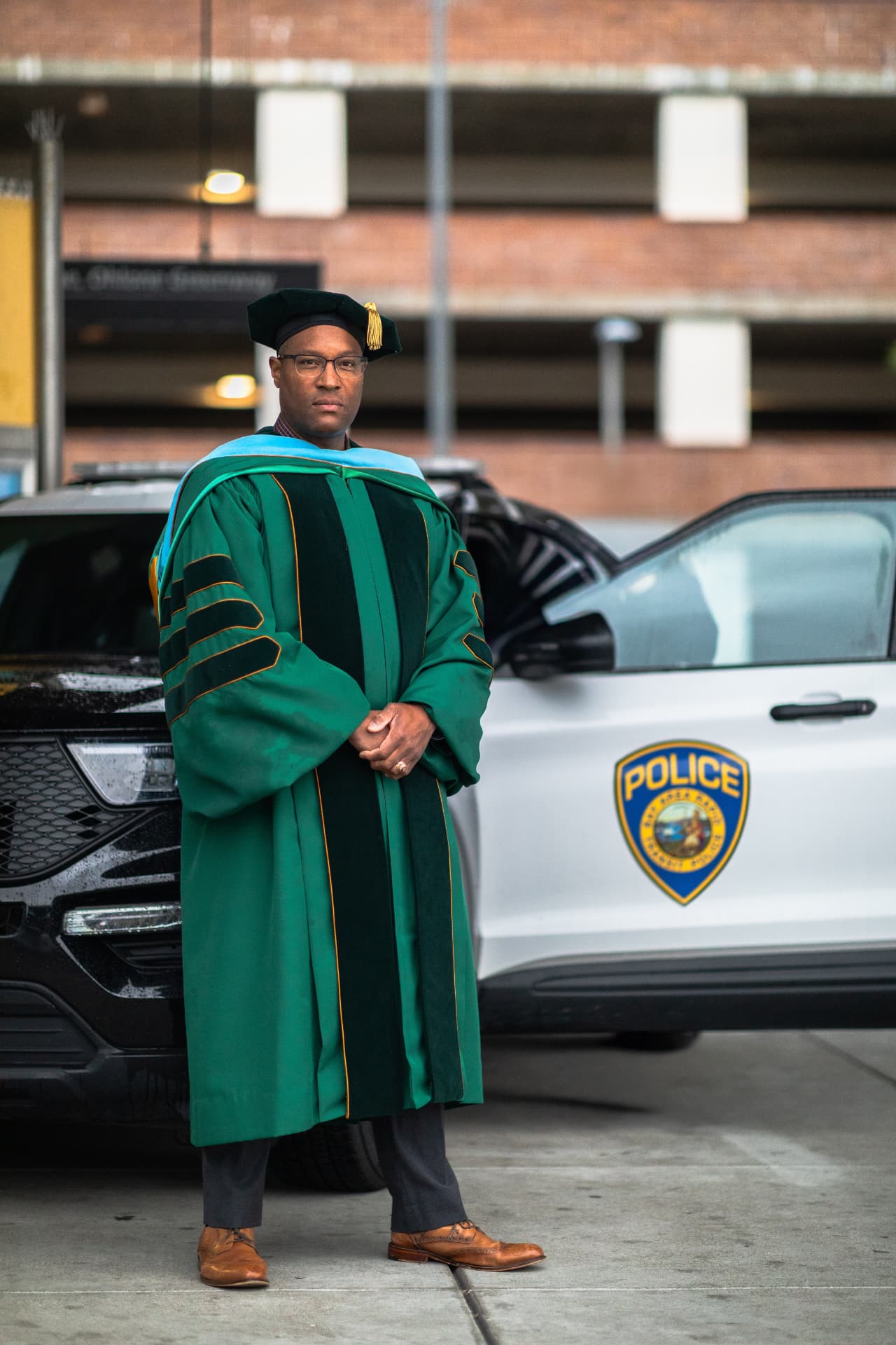 Quincy K. Ruffin in doctoral regalia standing beside a police patrol vehicle